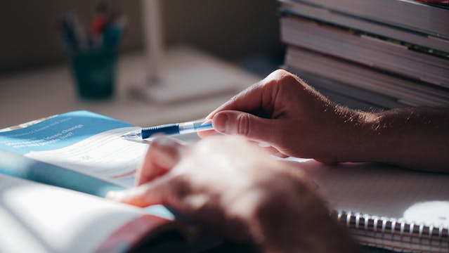 Pessoa estudando e fazendo anotações em livro aberto sob luz natural